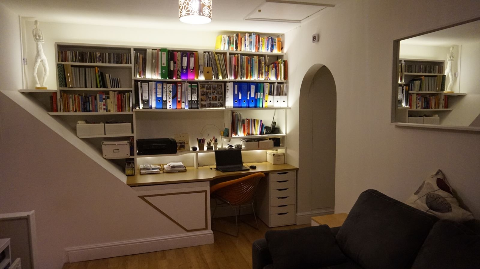 Wall-mounted shelving and desk following the angle of the stairs, lit and full of books