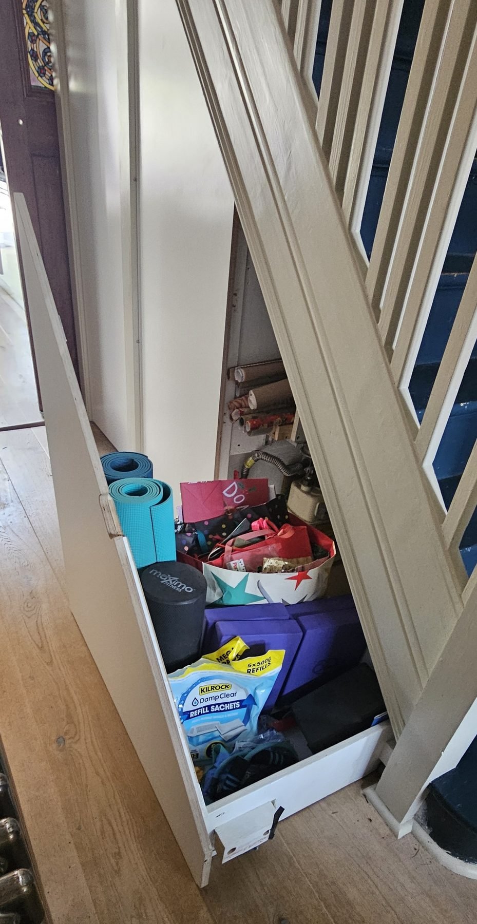 The understairs drawer pulled out, holding yoga mats, gift bags and wrapping paper
